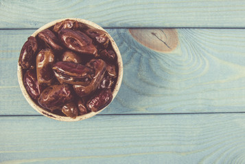 Dry dates fruit in the bowl, on the wood background.