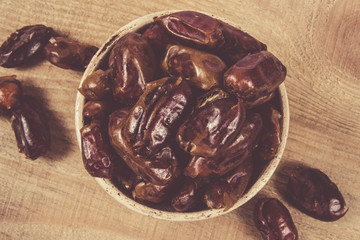 Dry dates fruit in the bowl, on the wood background.