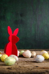 Easter bunny on old wooden table with colorful eggs. Dark background. Copy space.