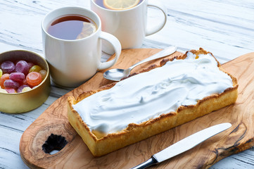 Tea time. Two cups of English black tea with lemon, a beautiful cake and a tin box with differently made lollipops. Pie with protein cream on an exquisite wooden board, a teaspoon and a dessert knife.