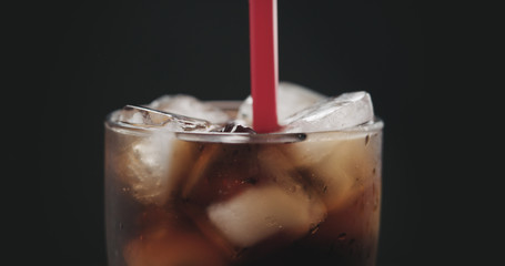 red straw in cola with ice cubes in glass over black background