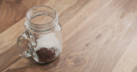 making cocoa drink in glass jar with handle on wood table, adding sugar
