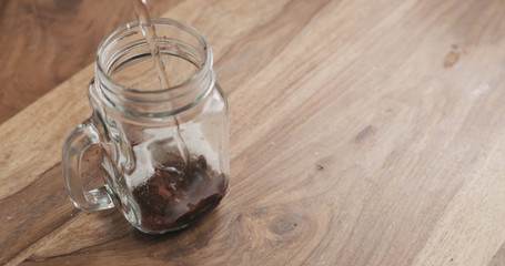 making cocoa drink in glass jar with handle on wood table, adding water