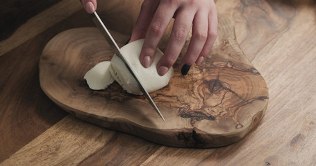 young female hands slicing mozzarella cheese on wooden board