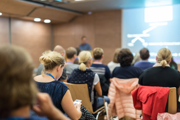 Business and entrepreneurship symposium. Speaker giving a talk at health care workshop meeting. Audience in conference hall. Rear view of unrecognized participant in audience.