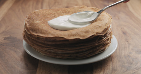 spreading sour cream on top of pancakes or blini