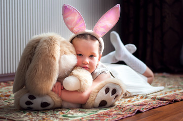 Cute little child wearing bunny ears on Easter day. Girl lying near toy rabbit.