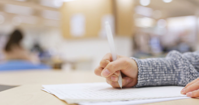 Student doing her homework, writing on note in library