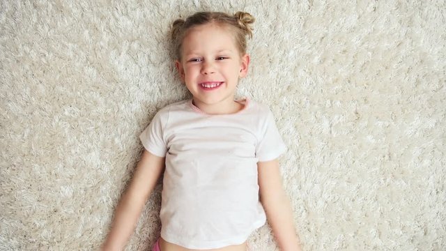 Adorable playful girl imagining fly, lying on carpet indoors. Cute little girl having fun at home. 