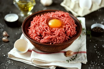 Minced beef meat with sea salt, pepper on a black background.