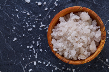 Large white sea salt in a natural wooden bowl on dark background, top view, close-up, selective focus