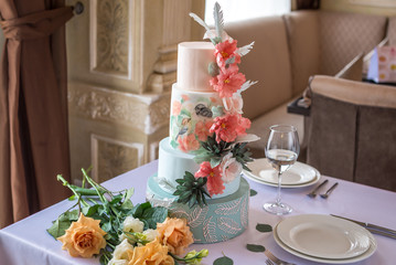 Home wedding for-tiered cake on the table in the restaurant decorated with pink roses and green leaves in a rustic style