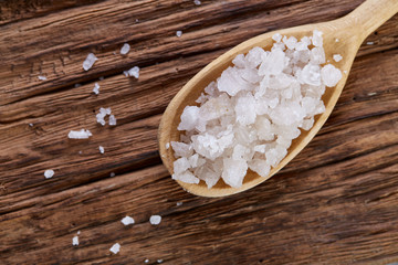 Obraz na płótnie Canvas Crystal sea salt in a wooden spoon on dark vintage wooden background, top view, close-up, selective focus.