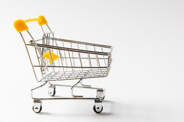 Close up of supermarket grocery push cart for shopping with black wheels and yellow plastic elements on handle isolated on white background. Concept of shopping. Copy space for advertisement