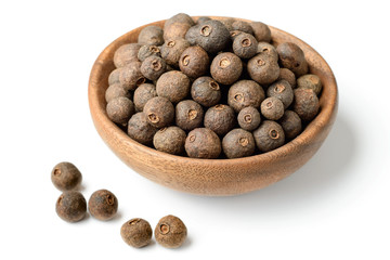 dried allspice in the wooden plate, isolated on white background