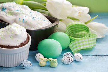 Easter holiday concept-Easter cakes,Easter eggs,bunnies,white tulips and green ribbon on blue wooden board.Template for greeting cards.