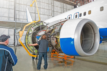 Assembling, replacing engine parts of the aircraft after repair. Specialist mechanic controls the crane when assembling an engine on the wing of an airplane. Concept maintenance of aircraft.