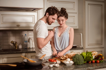 Female and male vegeterians stand together against kitchen interior, prepare vegetable salad....
