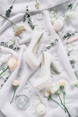 Wedding stylish composition with high heel shoes, eucalyptus branches, rose flowers on white textile background. Flat lay, top view festive wedding fashion concept.