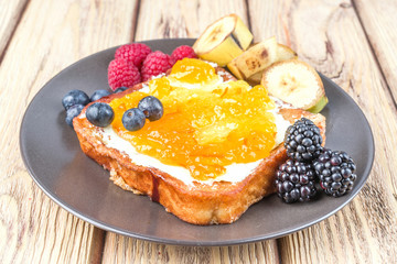 French toast with fried banana and berries spread on butter and jam, on natural wood