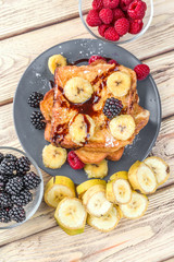 vertical shot of a tower of french toast with fried plantain and berries in natural wood