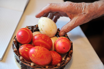 Older woman's hand taking easter traditional eggs (red and white) out of a small woven basket..