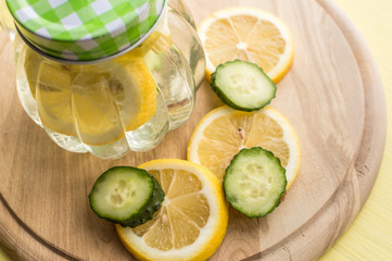 water with lemon and cucumber on wooden board with lemon and cucumber slices