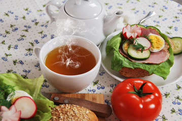 hot tea in a cup for breakfast with healthy sandwiches with lettuce, cucumber, egg, ham and radish flower with fresh dill