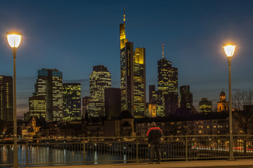  A photographer stands on the bridge and photographs the skyline of Frankfurt am Main at the blue hour. Concept: architecture or travel and vacation