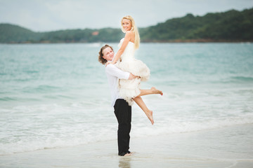 groom lifted his bride from sea. happy newlyweds on a deserted beach.