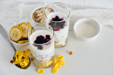 Breakfast in glass Cup: homemade granola, banana, fresh berries, yogurt on white background. The concept of healthy eating, high-carbon Breakfast.