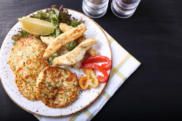 Fried fish with zuccini pancakes  on dark background
