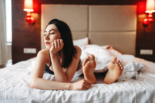 Woman in underwear lying in bed against male feet