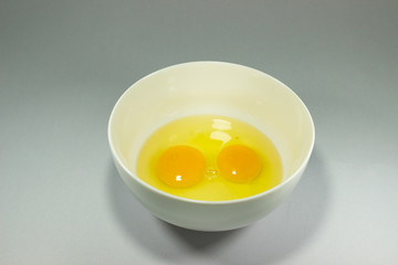 Two eggs in a white bowl on a gray background.