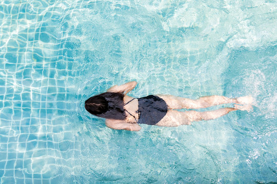 Top view of young attractive Asian woman in a swimsuit is swimming and in the transparent blue swimming pool.