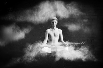 A man doing yoga in a white cloud of dust in a dark room. The concept of energy. Black-and-white photo. levitating in the Lotus position