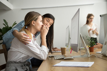 Asian colleague embracing supporting caucasian woman reading bad news in email, teammate comforting...