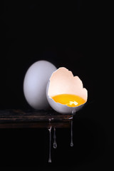 Egg with yolk and drops on the edge of a wooden table.