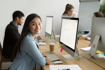 Smiling asian office employee looking at camera working with multiracial colleagues, happy young...
