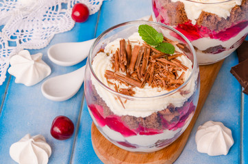 English trifle with chocolate biscuit, whipped cream, cherry and meringue in glass