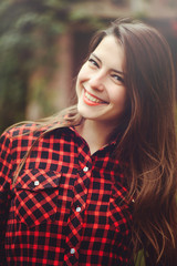 Fototapeta premium Smiling young brunette woman posing in the courtyard of her residence in a red checkered shirt is happy, portrait happy carefree, health in cushy tones