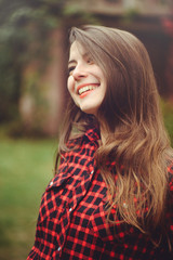 Smiling young brunette woman posing in the courtyard of her residence in a red checkered shirt is happy, portrait happy carefree, health in cushy tones