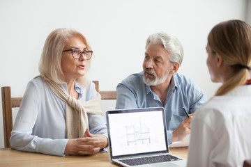 Senior couple talk to real estate agent about house purchase at meeting, interior designer advisor consulting older family with home plan on laptop screen, aged man and woman negotiating with realtor
