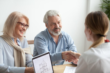 Smiling satisfied senior couple making sale purchase deal concluding contract handshaking real...