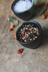 Close up view of spices, coarse salt and colorful allspice pepper in ceramic bowls, bay leaves and dried chilly peppers on old rustic wooden background. Vintage toned. Spices background