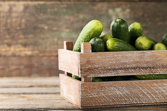 Fresh cucumbers in crate on grey wooden table