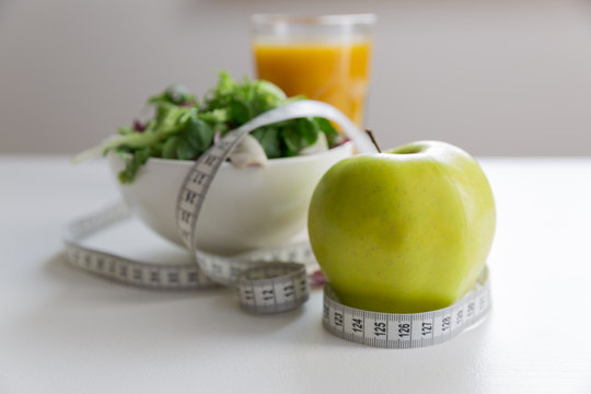 Measuring tape around the apple, bowl of green salad and glass of juice. Weight loss and right nutrition concept