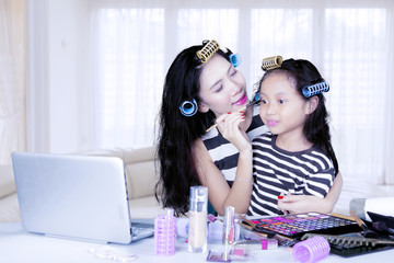 Mother and daughter with hair curler watching makeup tutorial on laptop computer