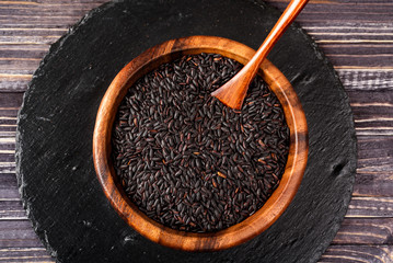 Isolated handful of raw black (nero) rice in the wood bowl on black stone background