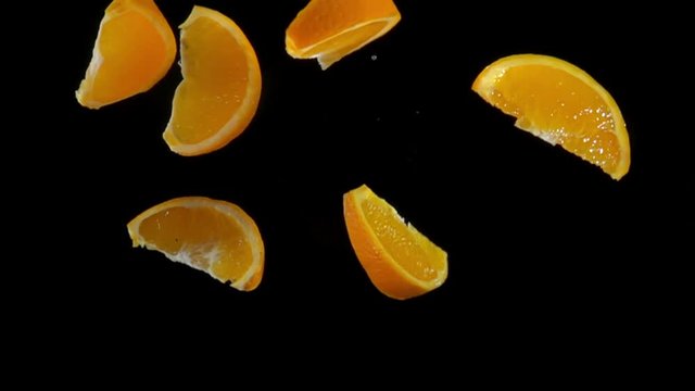 Slices of orange flies to the camera on a black background in slow motion